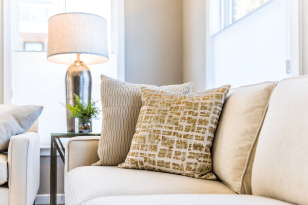 Closeup of two pillows on couch or sofa by bright window in modern home with staging of large beige, neutral white colors, lamp
